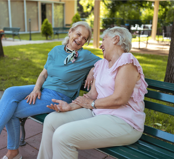 Two Senior Women Enjoying Together While Sitting on Bench in Park of Retirement Home, Retirement Age