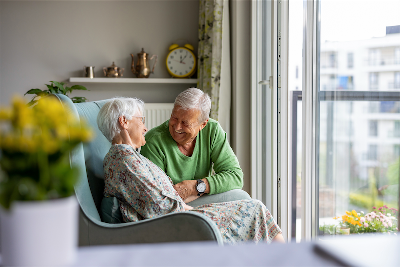 Senior woman and man sitting in a chair looking out the window
