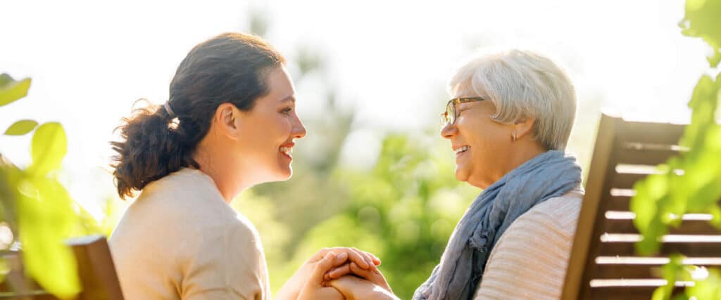 Happy young woman and her mother relaxing in summer morning. Family sitting in the garden and enjoying the conversation.
